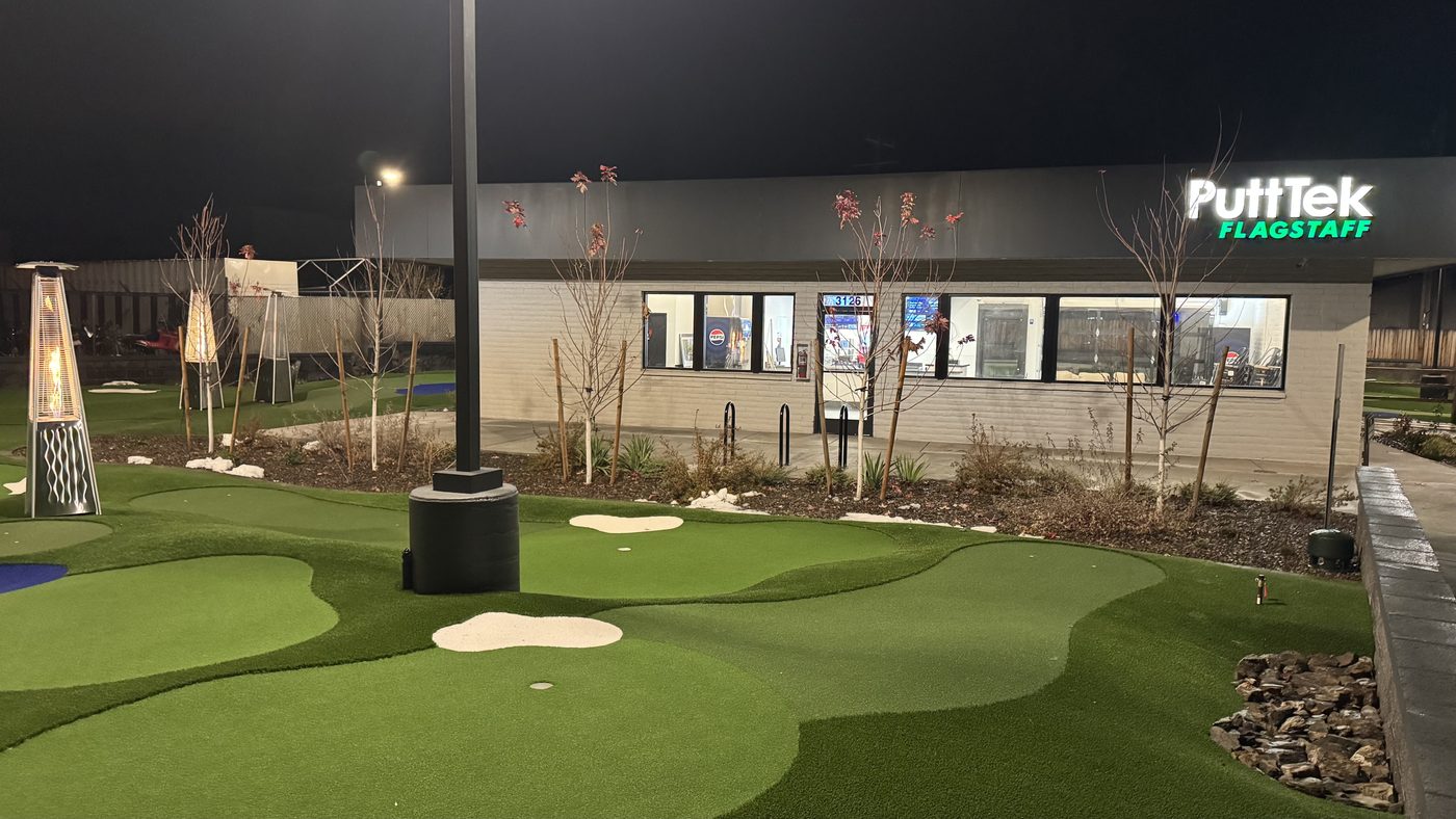 The PuttTek Flagstaff clubhouse building at night with the greens and patio heaters in the foreground.